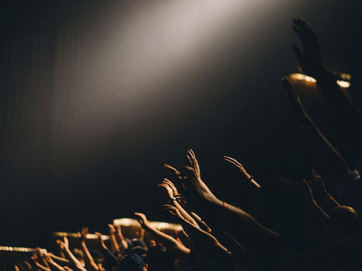 A group of hands reaching upwards in a dark setting with a spotlight shining down from above.