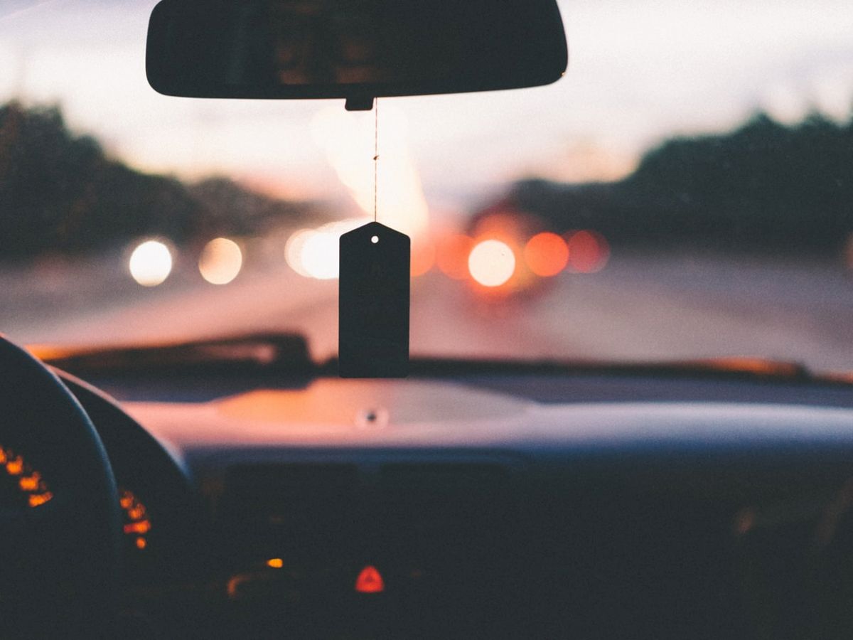 This is a view from inside a moving car, showing a hanging air freshener and blurry lights outside through the windshield as the car drives.