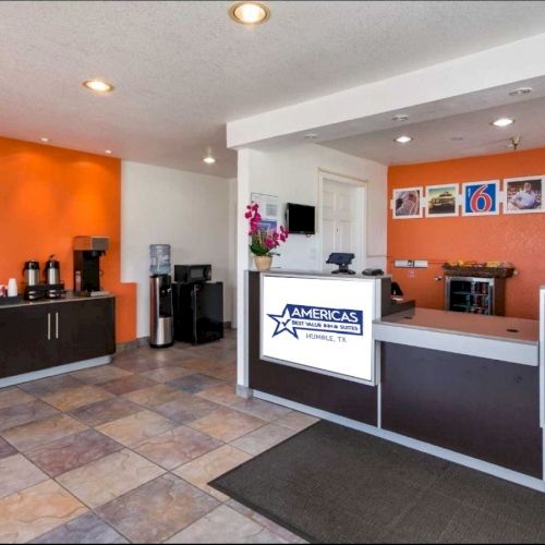 A hotel reception area with an orange wall, a coffee station, a water dispenser, and signage for 