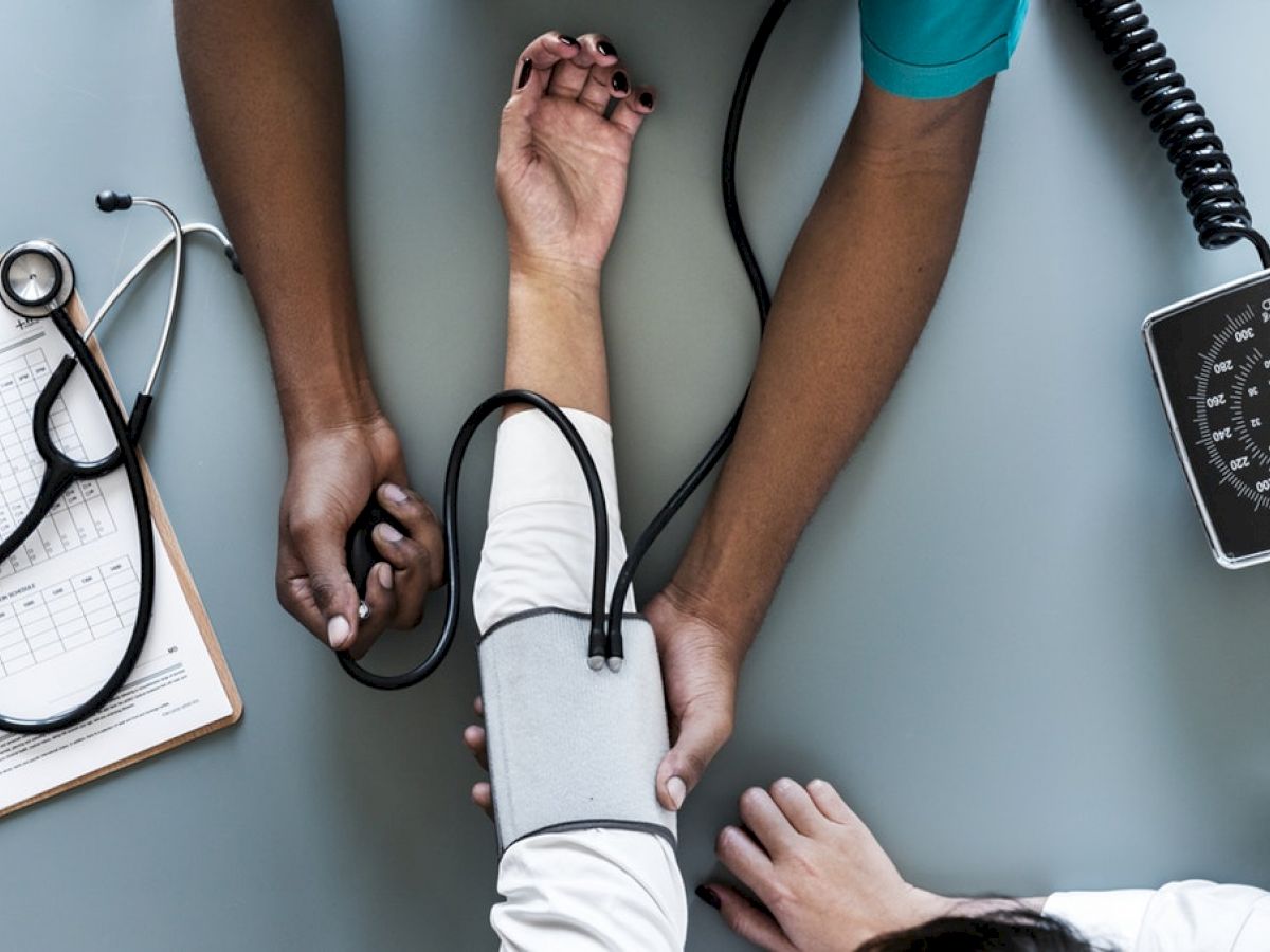 A healthcare professional is checking a patient's blood pressure using a sphygmomanometer; a clipboard and stethoscope are also visible.