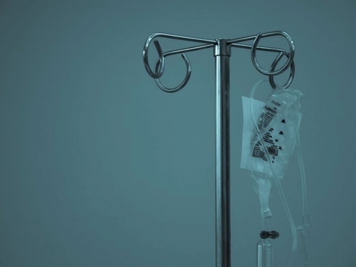 An IV pole with a hanging intravenous fluid bag and attached tubing is shown against a muted blue background.