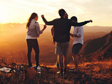 Four people standing on a hill during sunset, with one person spreading their arms out. There are some items on the ground.