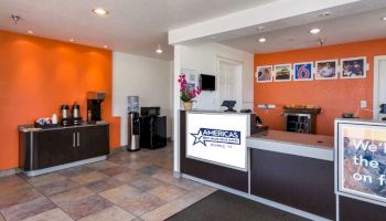 This image shows a hotel lobby with a reception desk, a coffee station, and a seating area. The walls are orange and decorated with pictures.