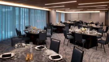 This image shows an elegantly set banquet hall with round tables, black tablecloths, floral centerpieces, and cushioned chairs, ready for a formal event.