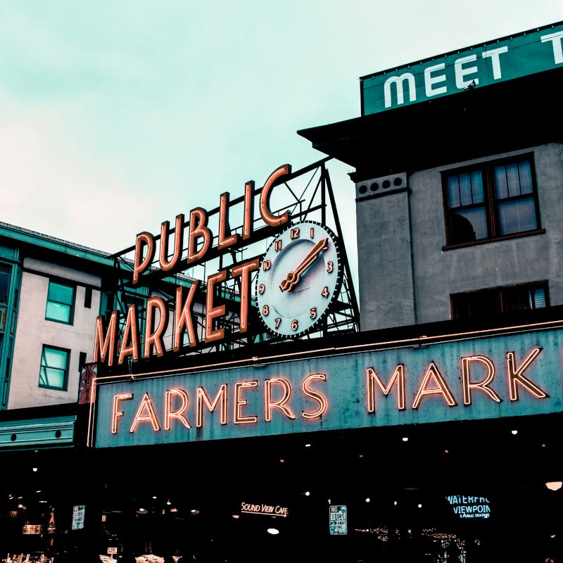 This image shows the iconic sign of Pike Place Market in Seattle with "Public Market" and "Farmers Market" written on it, including a clock.
