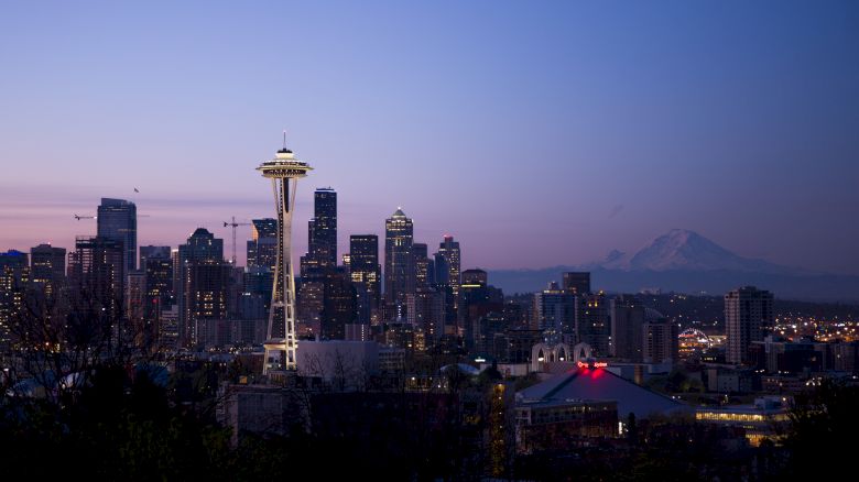 This image showcases the Seattle skyline at dusk, featuring the Space Needle prominently with Mount Rainier in the background.